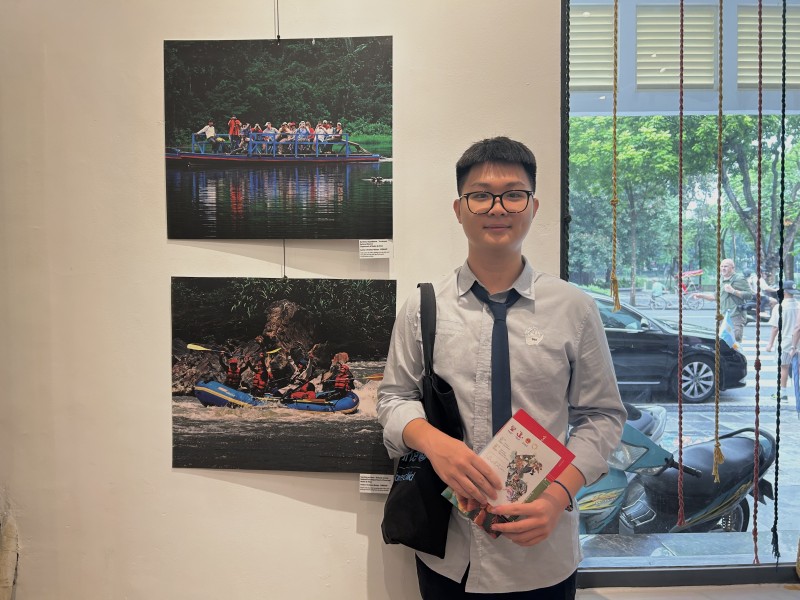Nguyễn Đức Huy bên cạnh bức ảnh  “Kayaking on rivers” mà em ấn tượng tại triển lãm. (Ảnh: Thu Phượng)
