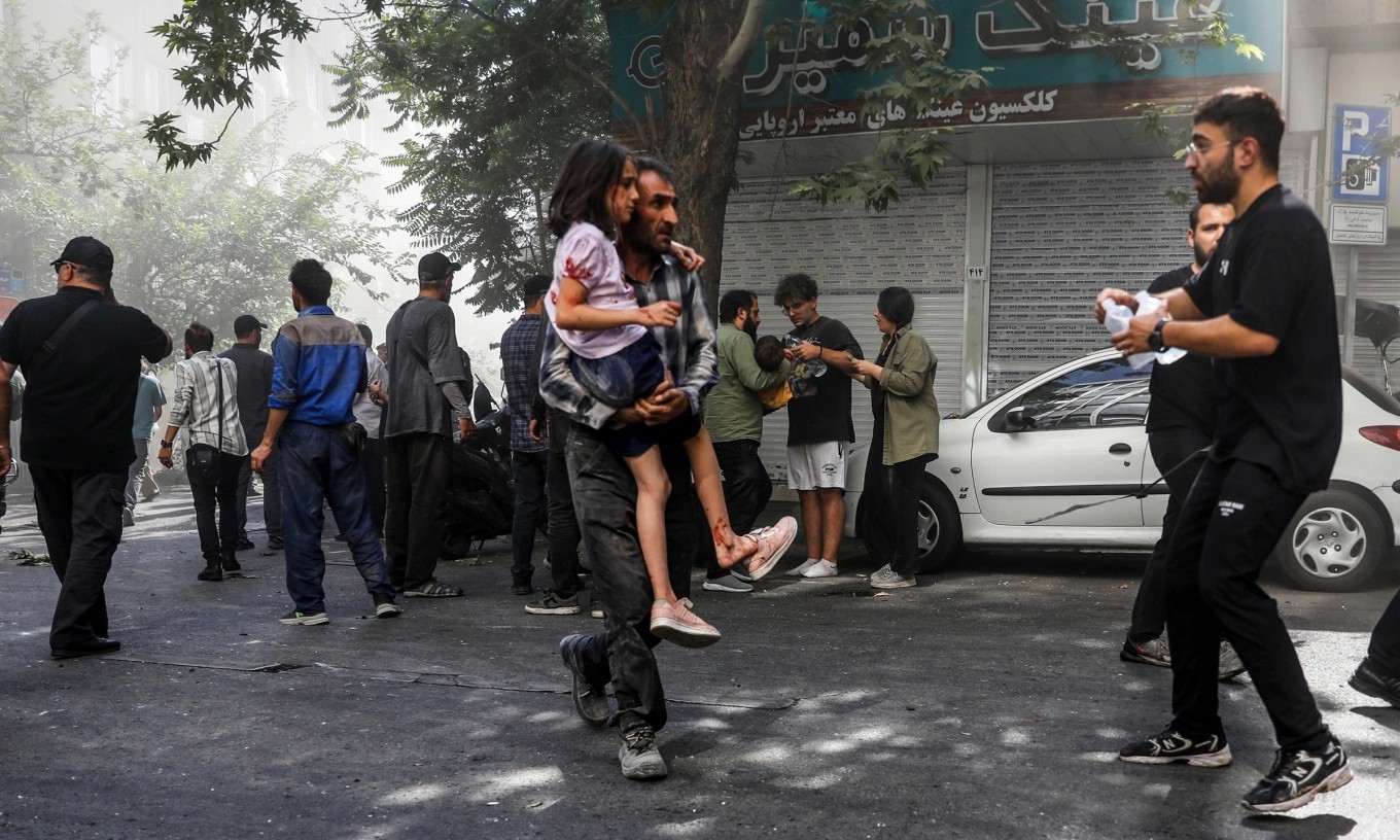 Người đàn ông bế bé gái bị thương sau cuộc không kích của Israel vào Tehran hôm 15/6. (Ảnh: AP)